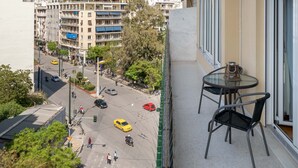 A balcony with a table and chairs, overlooking a street with cars and buildings.