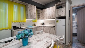 A kitchen with white wooden cabinets, a white countertop, a sink, and a dining table with chairs. There is a vase with flowers on the table.
