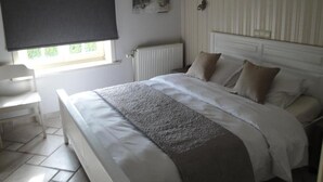 Un dormitorio con cama, radiador, ventana con persiana y una silla.