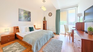 Un dormitorio con cama, mesitas de noche, escritorio, silla, radiador, televisor y ventana con cortinas.
