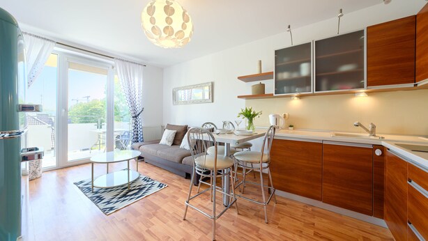 Una cocina moderna con armarios de madera, una mesa de comedor con sillas, y un sofá en un luminoso salón con vistas al exterior.