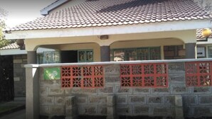 A house with a tiled roof, a stone wall with a decorative gate, and a small balcony. - The Reeds Hotel (Ongata Rongai)