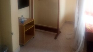 A small, dimly lit room with a wooden wardrobe, a mirror, and a bed with a sheer curtain. - The Reeds Hotel (Ongata Rongai)