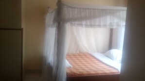 A single bed with a checkered bedspread, a white canopy, and a small round table beside it. - The Reeds Hotel (Ongata Rongai)