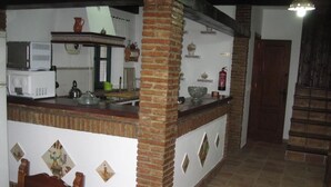 A kitchen with a brick column, white walls, and tiled floor. - The rural house Tigre (Gaucín)