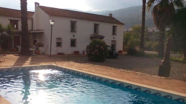 A swimming pool with clear water, surrounded by a paved area and a white building with multiple windows. - The rural house Tigre (Gaucín)