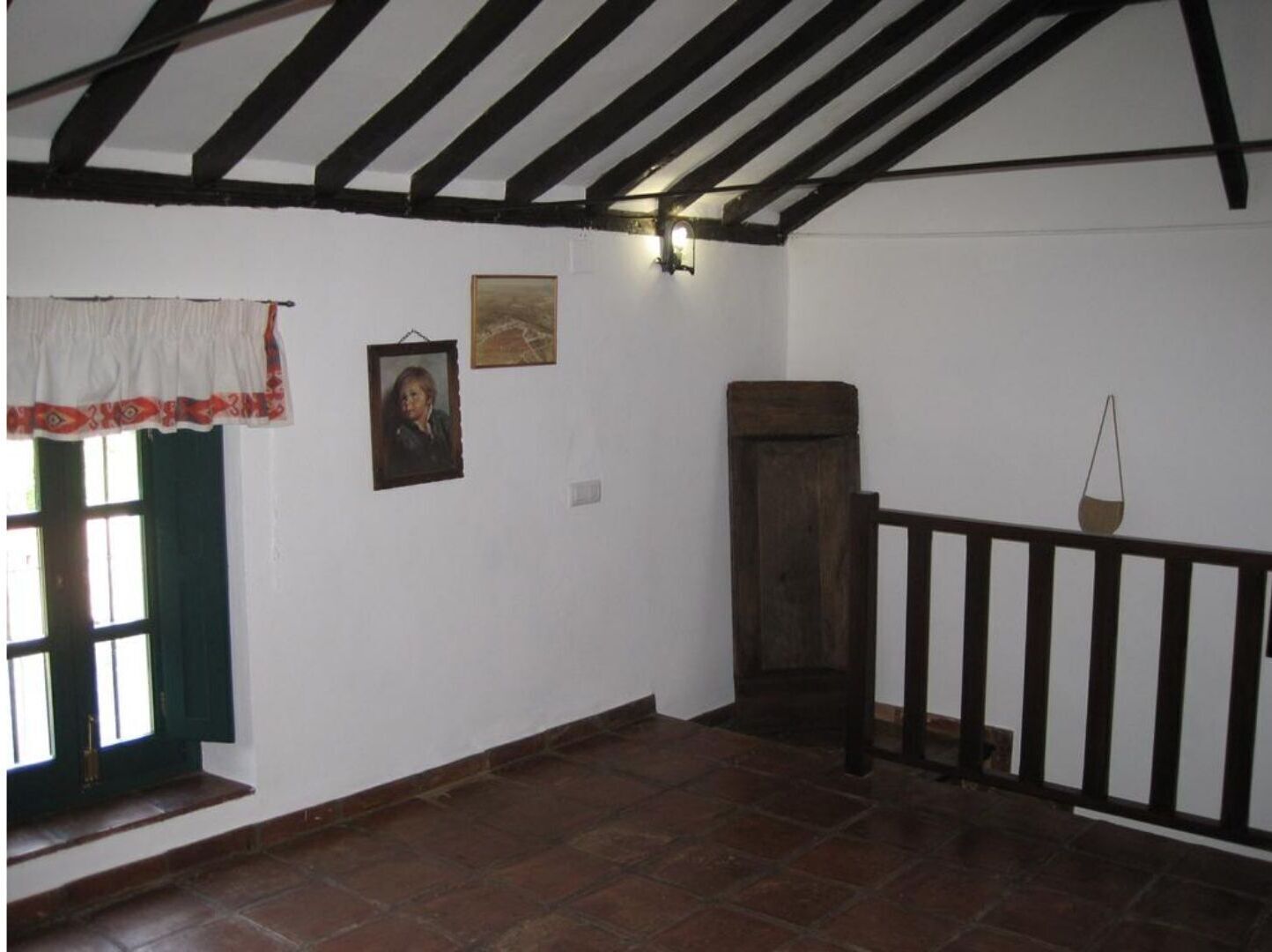 A room with a sloped ceiling, a wooden staircase, a window with a curtain, and a wall-mounted light fixture.