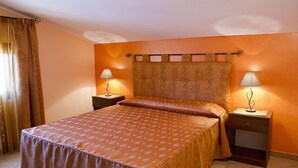 Ein Hotelzimmer mit einem großen Bett, zwei Nachttischen mit Lampen, einem Vorhang am Fenster und einer Kopfstütze mit Zierleiste.