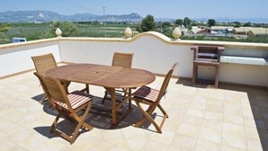 Eine Terrasse mit einem runden Tisch, Stühlen, einem Grill und Blick auf entfernte Gebäude und Berge.