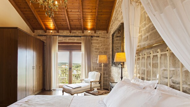 Een slaapkamer met een groot bed, een stoel, een nachtkastje en uitzicht op het omliggende landschap.