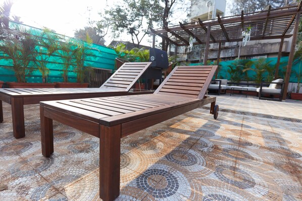 A wooden lounge chair with a backrest and armrests, positioned on a patterned tile floor.