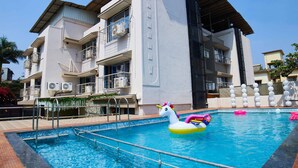 A swimming pool with a water slide and inflatable toys, surrounded by a building with balconies and air conditioning units. - Aureole Mrida (Mawal)