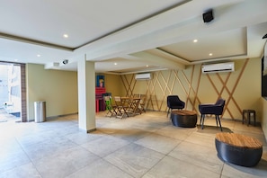 Un vestíbulo amplio con suelo de baldosas, una mesa de comedor de madera con sillas, un sofá de cuero negro y un taburete redondo de madera.