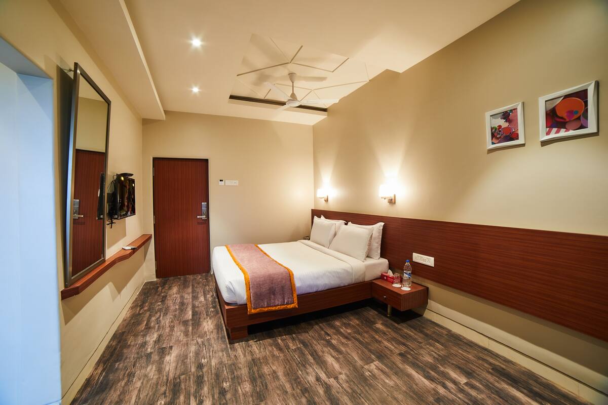 A hotel room with a large bed, a wooden headboard, a nightstand, a bedside table, a mirror, and a ceiling fan.