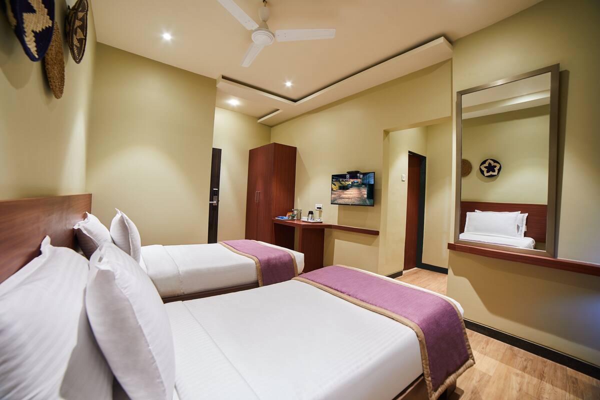 A hotel room with two beds, a television, a mirror, and a ceiling fan.