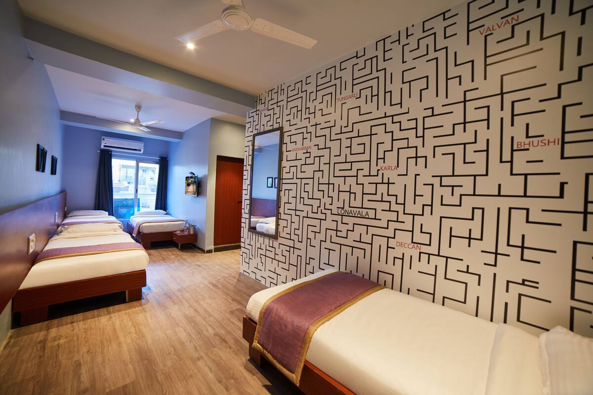 A hotel room with three beds, a ceiling fan, a wall-mounted TV, and a patterned wall.