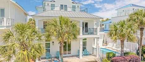A two-story residential building with a balcony, a pool, and outdoor seating.