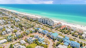 Vista aérea de una zona residencial costera con propiedades frente al mar, carreteras y un cielo azul despejado.