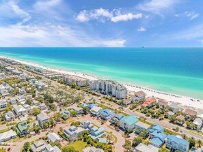 Vista aérea de una zona residencial costera con propiedades frente al mar, carreteras y un cielo azul despejado.