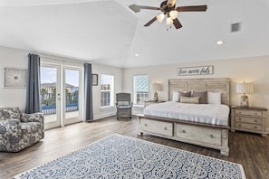 A bedroom with a bed, a chair, a nightstand, a ceiling fan, and a view through the glass doors.
