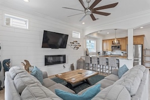 A spacious living room with a large sofa, a coffee table, and a television mounted on the wall.