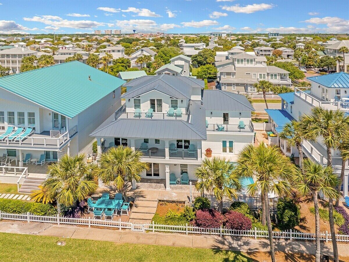 A coastal residential area with a large house featuring a balcony, a swimming pool, and palm trees.