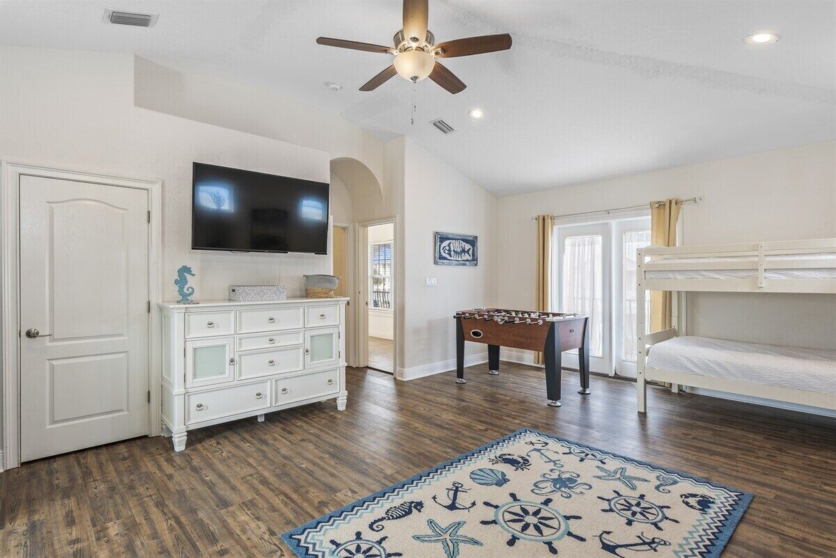 A room with a ceiling fan, a television, a foosball table, a bunk bed, and a decorative rug.
