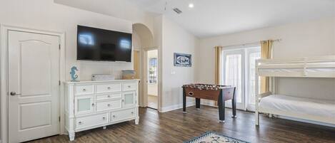 A room with a ceiling fan, a television, a foosball table, a bunk bed, and a decorative rug.