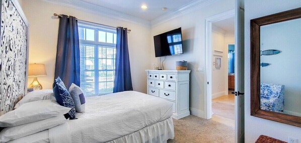 Un dormitorio con cama, cómoda, televisor y ventana con cortinas.