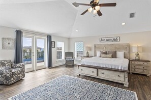 A bedroom with a bed, a chair, a nightstand, a ceiling fan, and a view through the glass doors.