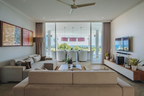 Ein modernes Wohnzimmer mit einer Couch, einem Essbereich mit Stühlen, einem Fernseher und Blick auf den Ozean.