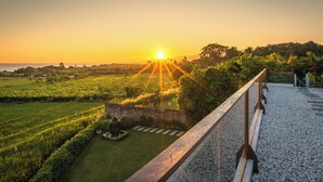 Vista al atardecer desde un balcón con muro de piedra, jardín y paisaje distante.