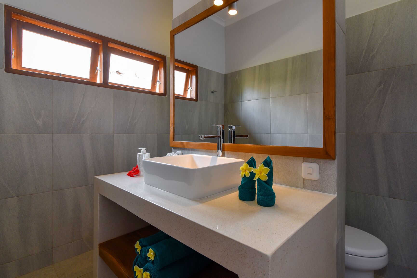 A bathroom with a white sink, a mirror, and a window above the sink.