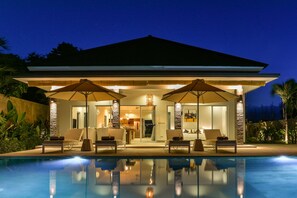 A modern house with a pool, outdoor seating, and a well-lit interior.
