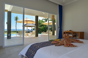 A hotel room with a large bed, a view of the ocean, and a patio area with lounge chairs and umbrellas. - Villa Saneva (Seririt)