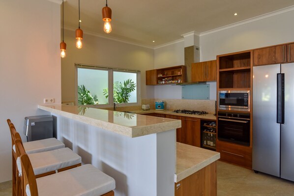 A modern kitchen with a central island, wooden cabinets, a built-in oven, and a stainless steel refrigerator.