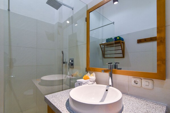 Une salle de bain moderne avec une douche à parois de verre, un lavabo rond et un grand miroir.