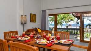 Ein Essbereich mit Tisch, gedeckt für das Frühstück, mit Blick auf einen Strand mit Palmen und den Ozean.