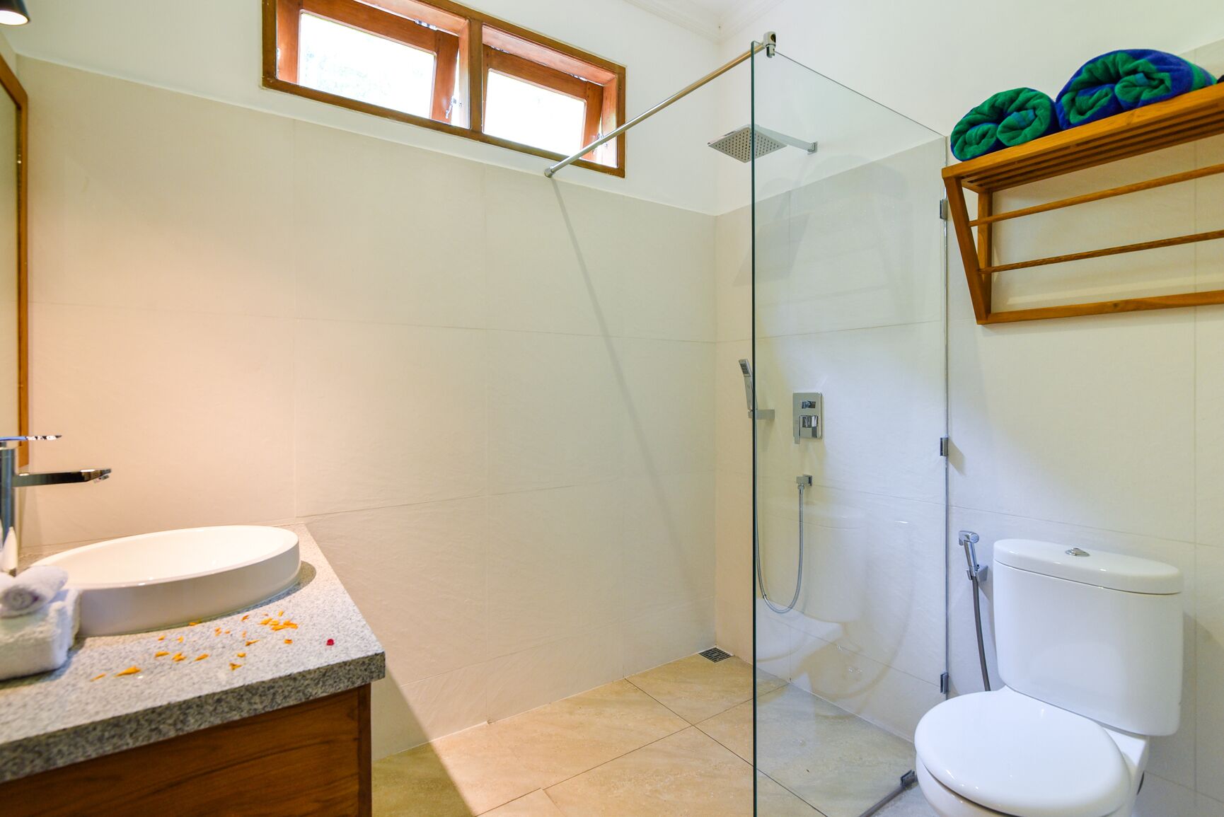 A bathroom with a glass shower enclosure, a toilet, and a sink with a towel on the counter.