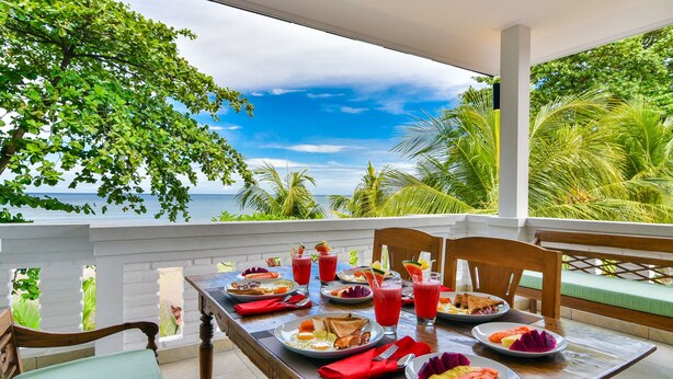 Une table à manger, dressée avec des aliments et des boissons pour le petit-déjeuner, sur un balcon donnant sur l’océan.