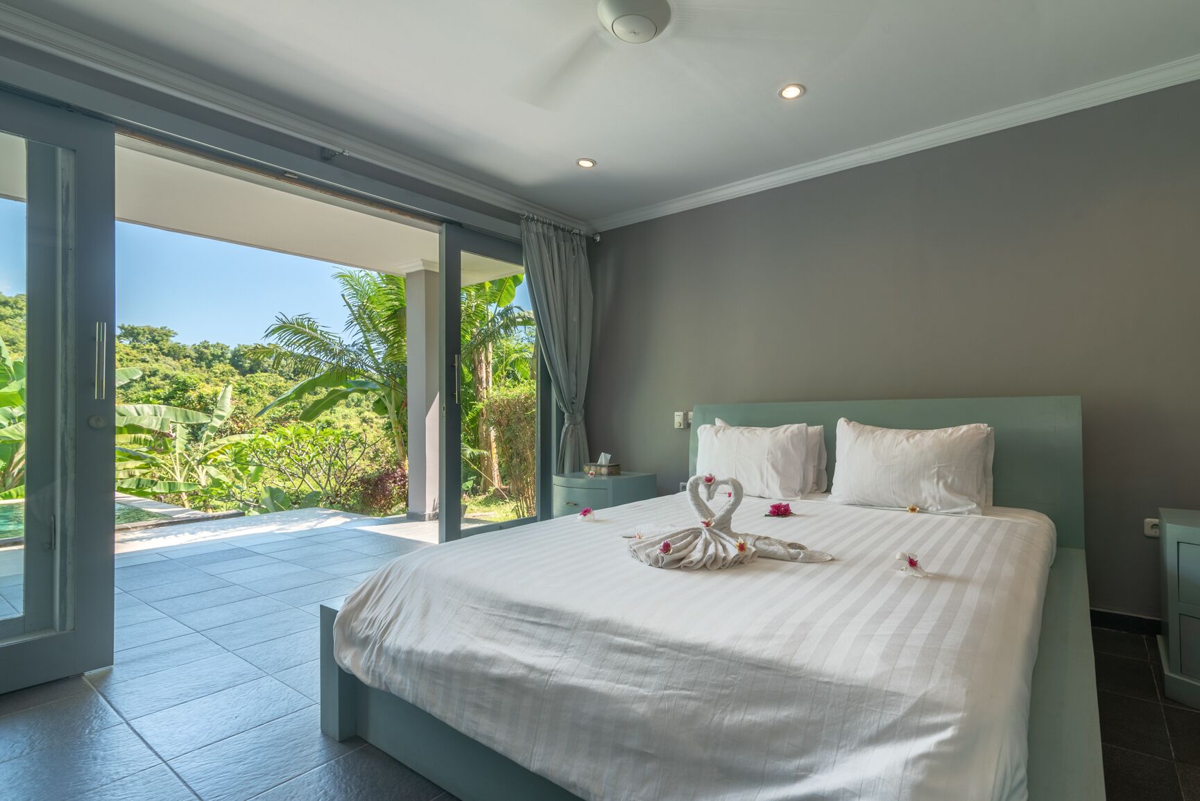 A spacious bedroom with a large bed, a view of lush greenery, and a sliding glass door leading to an outdoor area.