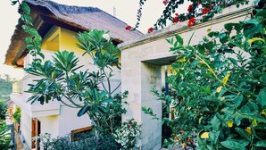 Ein traditionelles Gebäude mit einem strohgedeckten Dach, umgeben von üppiger Vegetation und blühenden Pflanzen.