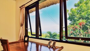 Ein Zimmer mit Holztisch, einem gerahmten Bild und Meerblick durch große Fenster.