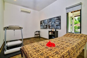 Un dormitorio con cama, cinta de correr, una silla y obras de arte en la pared.