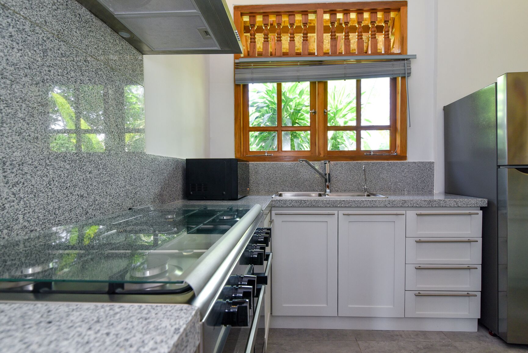A kitchen with a granite countertop, stainless steel appliances, a window with a wooden frame, and a view of greenery outside.