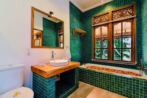 A bathroom with a wooden vanity, a round sink, a large window with a view of trees, and green tiled walls. - Villa Jintan (Sukasada)