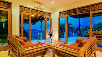 Una habitación con dos sofás de madera, una mesa y ventanas amplias con vistas a un paisaje montañoso.