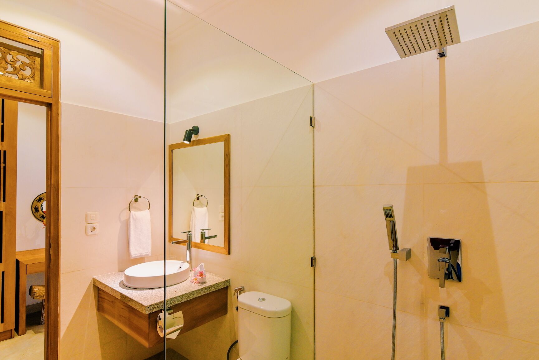 A modern bathroom with a glass partition, a wooden vanity, a sink, a toilet, and a shower.