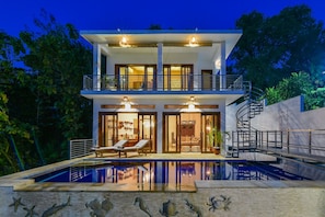 A two-story modern house with a swimming pool, a balcony, and a spiral staircase.