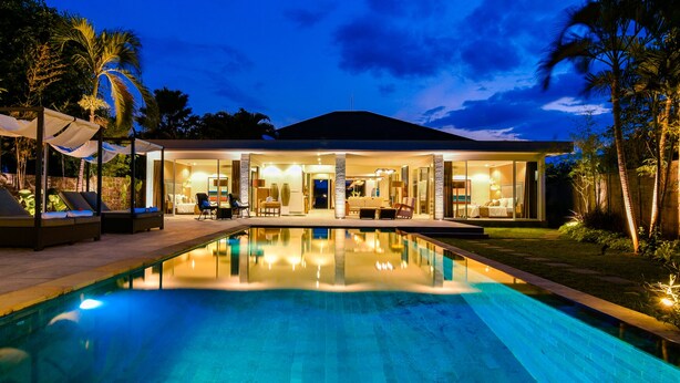 Una casa moderna con piscina, mobiliario exterior y un interior bien iluminado.